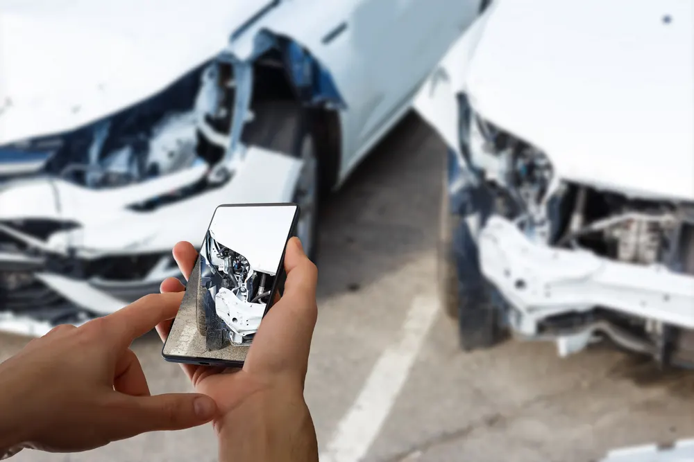 Mann fotografiert sein Fahrzeug mit Schadens- und Unfallversicherung mit Smartphone