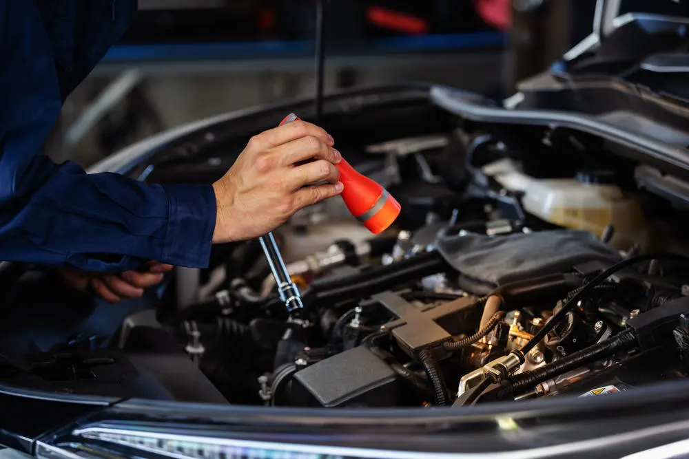 männliche Mechanikerin mit glänzender Taschenlampe zur Überprüfung eines Fahrzeugmotorenproblems