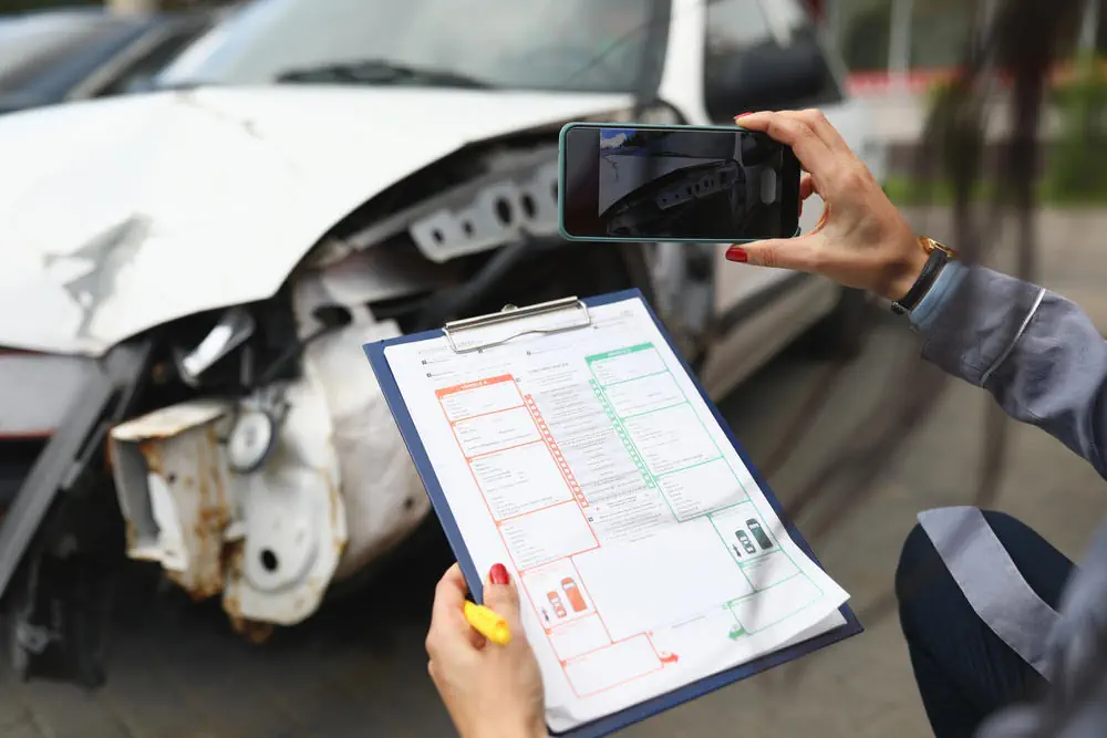 fotografieren ein kaputtes Auto mit Versicherungsdokumenten in den Händen